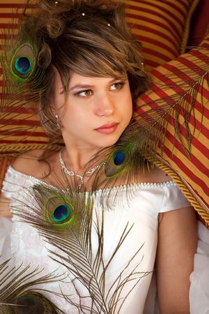 Pretty bride with the peacock feathers is laying on the pillows.の写真素材