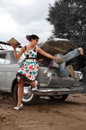Pretty couple is trying to repair their old car using manual. Rural background.の写真素材