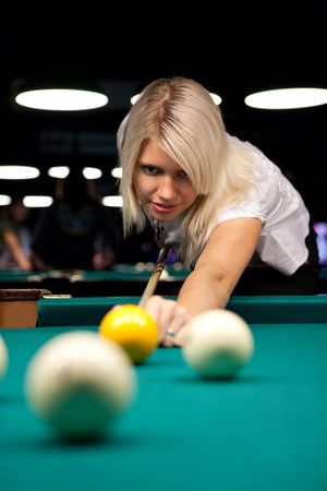 A blond girl is making a shot at a poolの写真素材