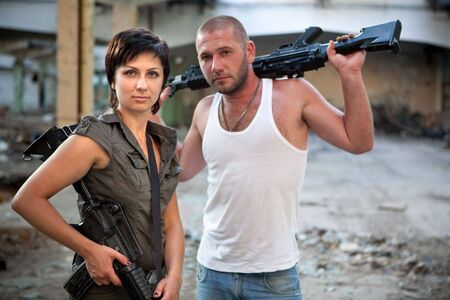 Armed couple with machineguns on the ruined building background.の写真素材