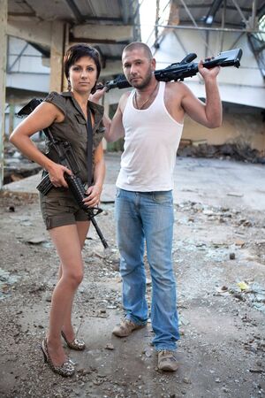 Armed couple with machineguns on the ruined building background.の写真素材