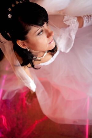 Pretty bride is sitting on the glass floor lighted with red. Focus point on the face.の写真素材