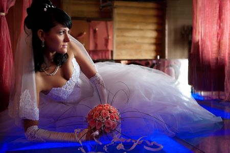 Pretty bride with bouquet is laying on the glass floor lighted with blue. Focus point on the face. の写真素材