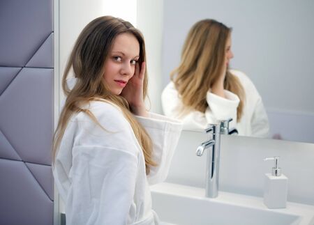 Pretty girl in the bathrobe is going to make a make-up near the mirrorの写真素材