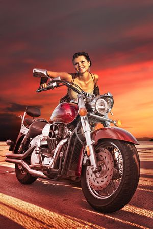 Sexy girl on the big chromed motorcycle on the sunset background.の写真素材