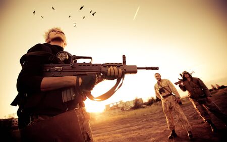 Blond woman with rifle is looking at ravens. Two rebels with machine gun on the background.