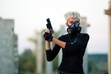 Blond woman in the gas mask with the pistol on the ruined background.の写真素材