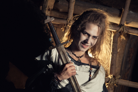 Pretty sorceress with the magic sword  Wooden den on the background の写真素材