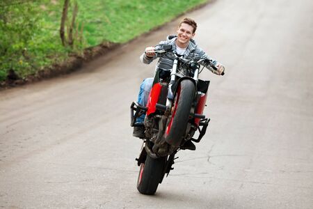 Stunt rider is riding on the one wheel of his motorbikeの写真素材