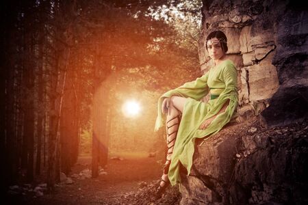 Elf woman is sitting on the rocks. Forest on the background.の写真素材