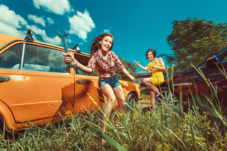 Cheerful woman mecanic is repairing a car with the wrench another woman is watching.の写真素材