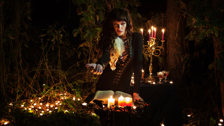 Beautiful witch with the vintage book of magic invites you into the forest.の写真素材