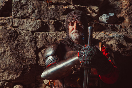 Old medieval King in armor with sword on the rocks background. Focus point on the face.の写真素材