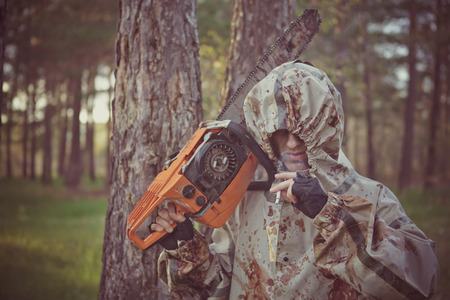 Smoking maniac with the chainsaw dressed in a dirty bloody raincoat. Low contrast post-processing.の写真素材