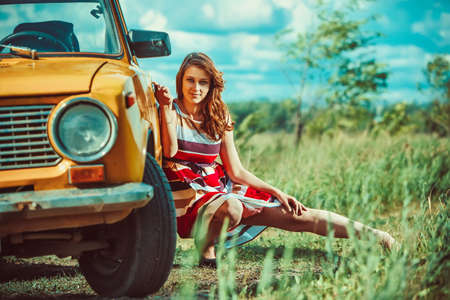 Beautiful woman near the old car. Blue sky and clouds on the background.の写真素材