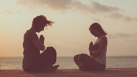 Young couple is doing yoga on the sunrise background. Artistic toning.の写真素材