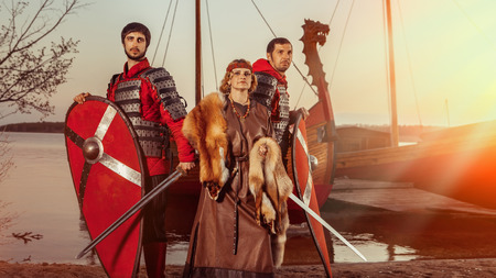 Slavic princess and two warriors with swords and shields on the warships background.の写真素材