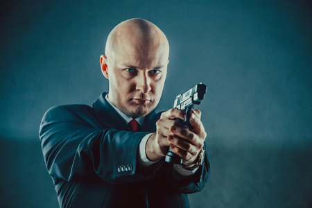 Bald man in business suit with the gun.の写真素材