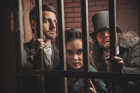 Two gentlemen and a lady behind bars in the prison.