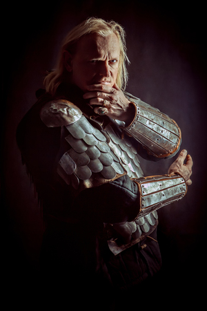 Powerful blond knight is standing with the crossed arms on the dark backgroundの写真素材
