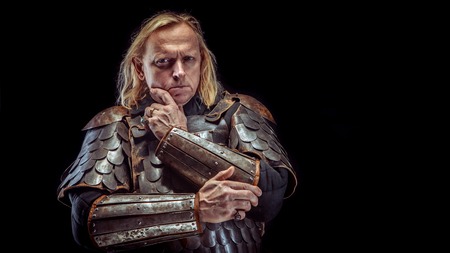 Powerful blond knight is standing deep in thoughts. Dark backgroundの写真素材