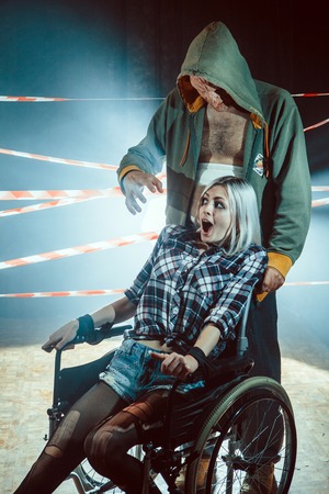 Maniac and his tied victim in the wheelchair on the dark background.