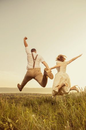 Attractive couple is jumping on the top of the hill. Sunset on the background.の写真素材