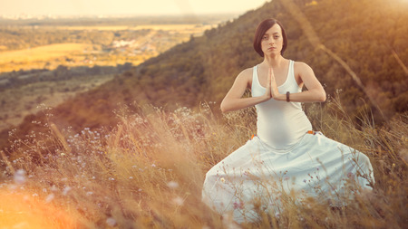 Pregnant woman practicing yoga pose, breathing exercise, stretching on nature outdoors.の写真素材