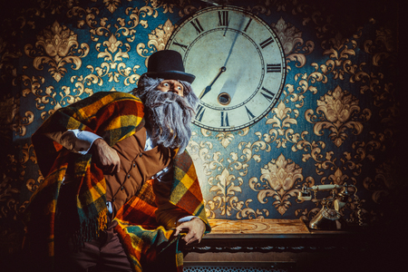 Senior caucasian man standing near wall clock in the dark room.の写真素材
