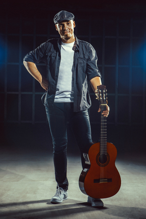 Street musician with playing guitar on the dark wall backgroundの写真素材