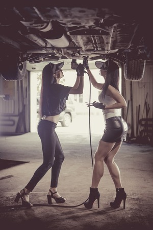 Two women mechanics are repairing a car on the lift.