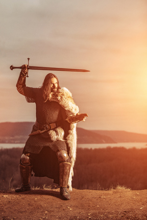 Long haired knight with the two-handed sword. Medieval rural background.の写真素材
