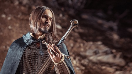 Long haired knight with the two-handed sword. Rocks on the background.の写真素材