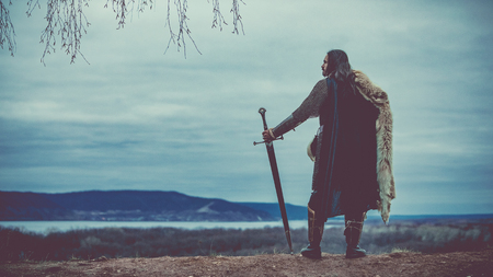 Long haired knight with the two-handed sword. Medieval rural background.