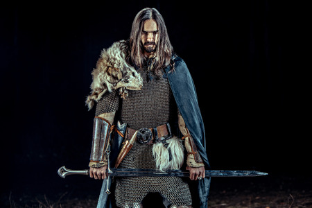 Long haired knight with the two-handed sword. Rocks on the background.の写真素材