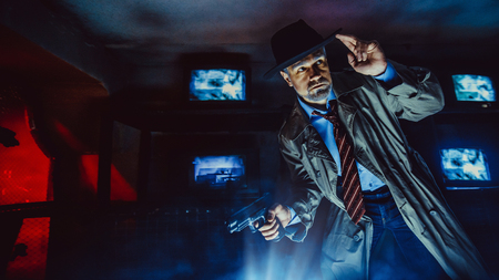 Detective with the gun wearing a fedora hat and a trench coat, dark background.の写真素材