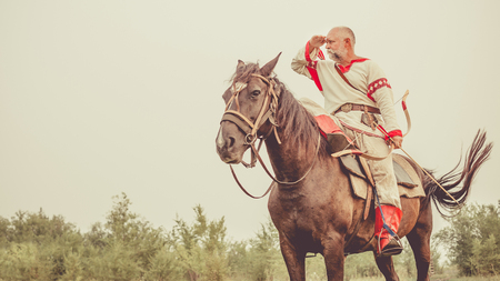 Man in ethnic clothing with the bow is riding a horse and searching for enemy.の写真素材