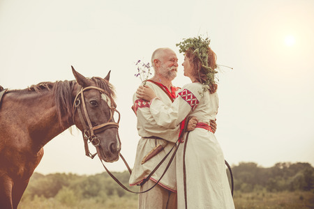 Mature man and woman in ethnic clothes are going to make a horse ride on the rural summer background.の写真素材