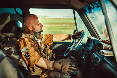 Bald soldier in uniform is driving military vehicle.