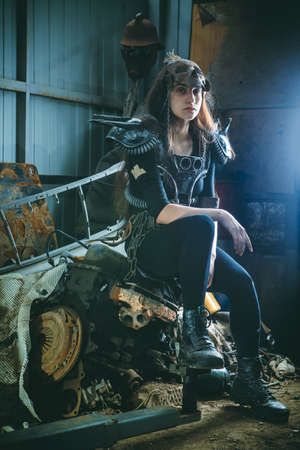 Post apocalyptic woman warrior in armor is sitting on the rusty engine.の写真素材