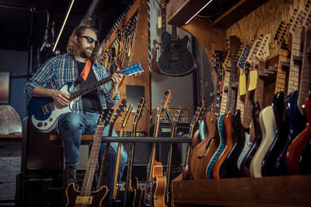 Guitarist is playing on electric guitar in a musical instrument shop.