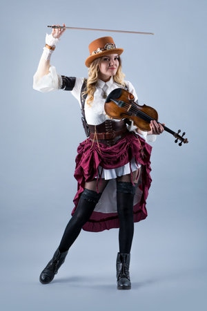Country girl with violin. Woman with violin on grey background. Woman in western style with violin. Cowgirl with hat playing the violin country music standing on grey background.の写真素材