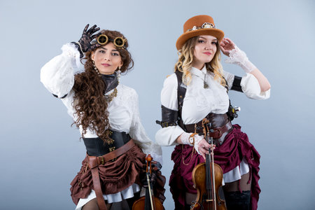 Country girls with violins. Women with violins on the grey background. Women in western style with violas. Cowgirls playing violins country music.の写真素材