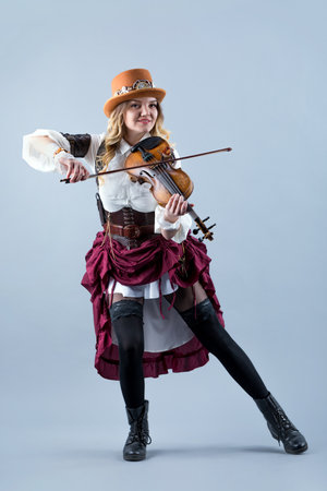 Country girl with violin. Woman with violin on grey background. Woman in western style with violin. Cowgirl with hat playing the violin country music standing on grey background.の写真素材