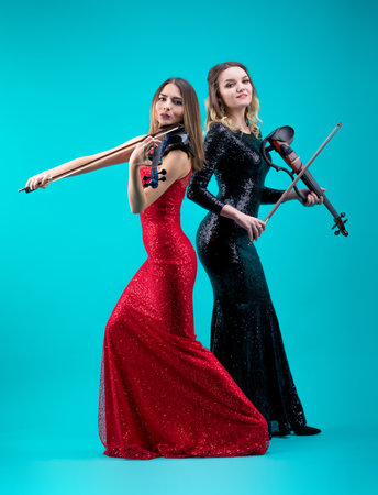 Violinist women duet in the evening gowns on the blue background.の写真素材