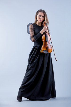 Violinist woman in the evening gown on the grey background.の写真素材