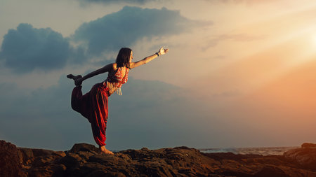 Young beautiful healthy woman making meditation on the rocks, sunset on the sea. Arambol, Goa, India.の写真素材