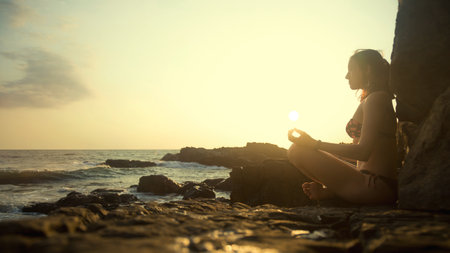 Young beautiful healthy woman making meditation on the rocks, sunset on the sea. Arambol, Goa, India.の写真素材