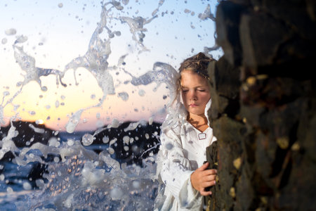 Little girl dreaming in the spray of waves at sea on a sunset background.の写真素材