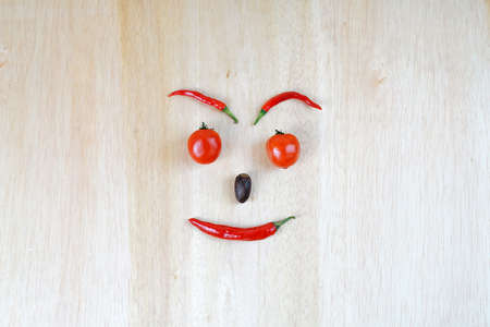 red chili shaped like a human head on a brown wooden plank backgroundの写真素材